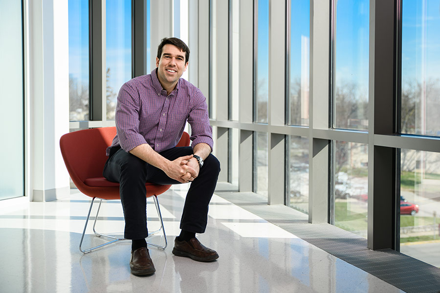 An MBA student sits in a red chair against a wall of windows that overlook the Indiana University Bloomington campus.